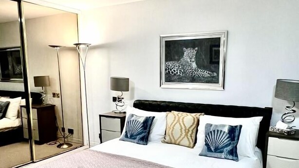 A hotel room with a bed, a large mirror, a framed artwork, and bedside lamps. - Mayfair Piccadilly Apartment (London)