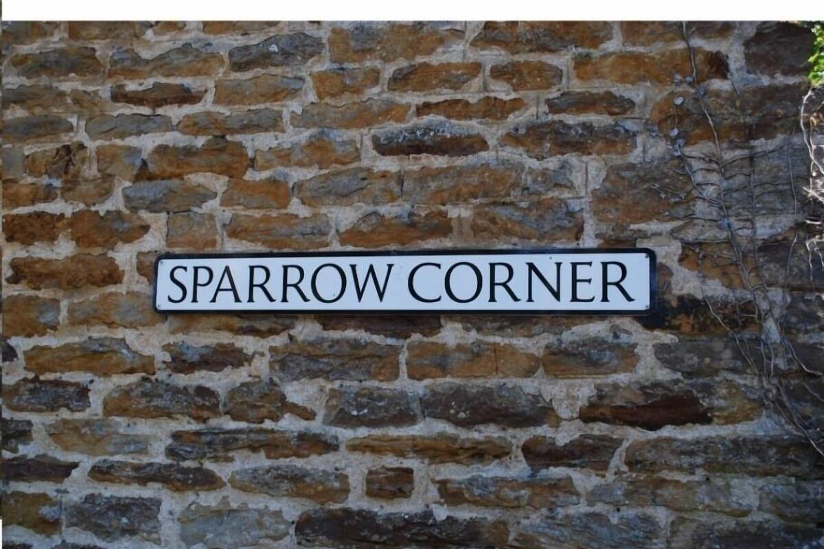 A sign reading "SPARROW CORNER" on a stone wall.