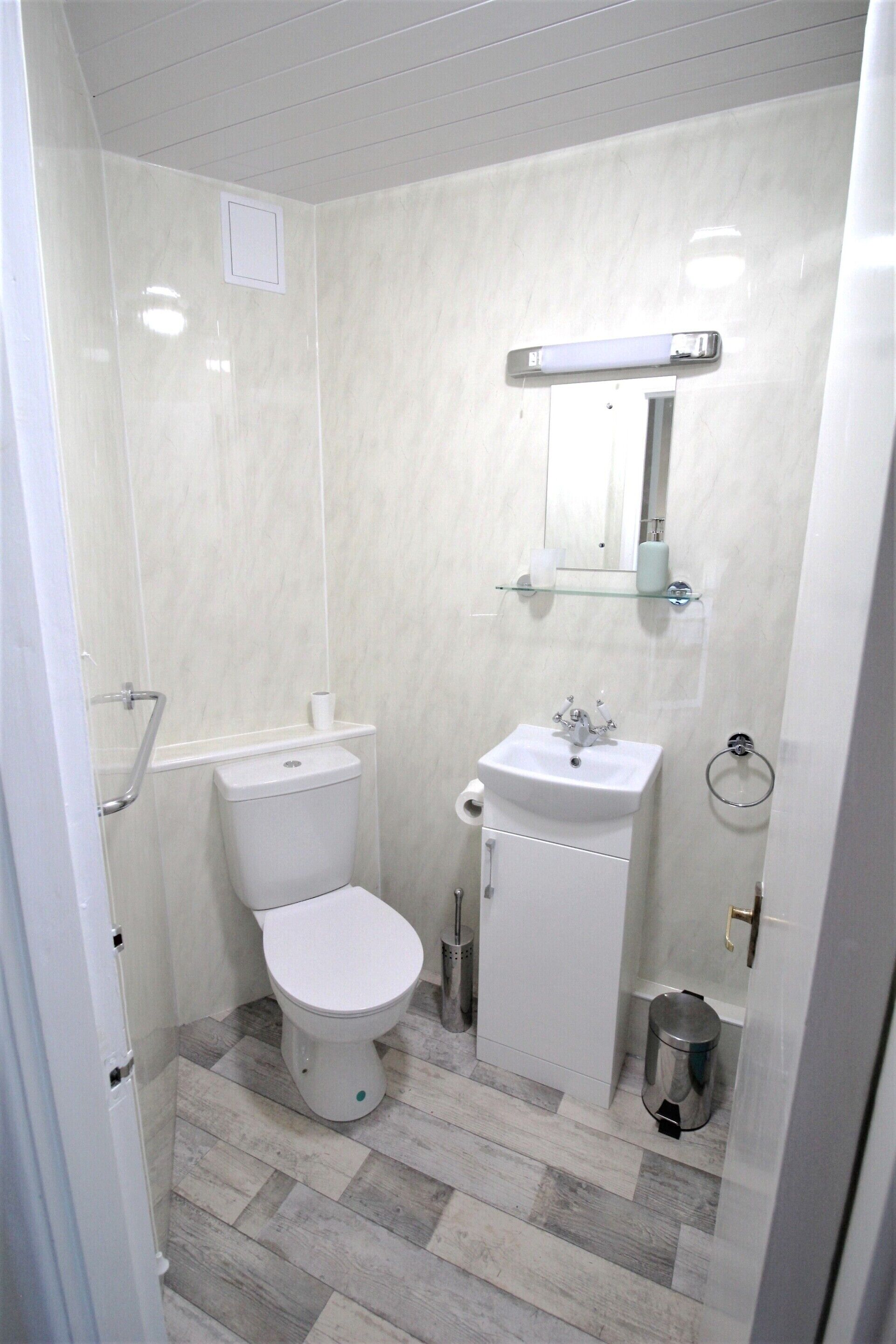A bathroom with a toilet, sink, mirror, and trash can.
