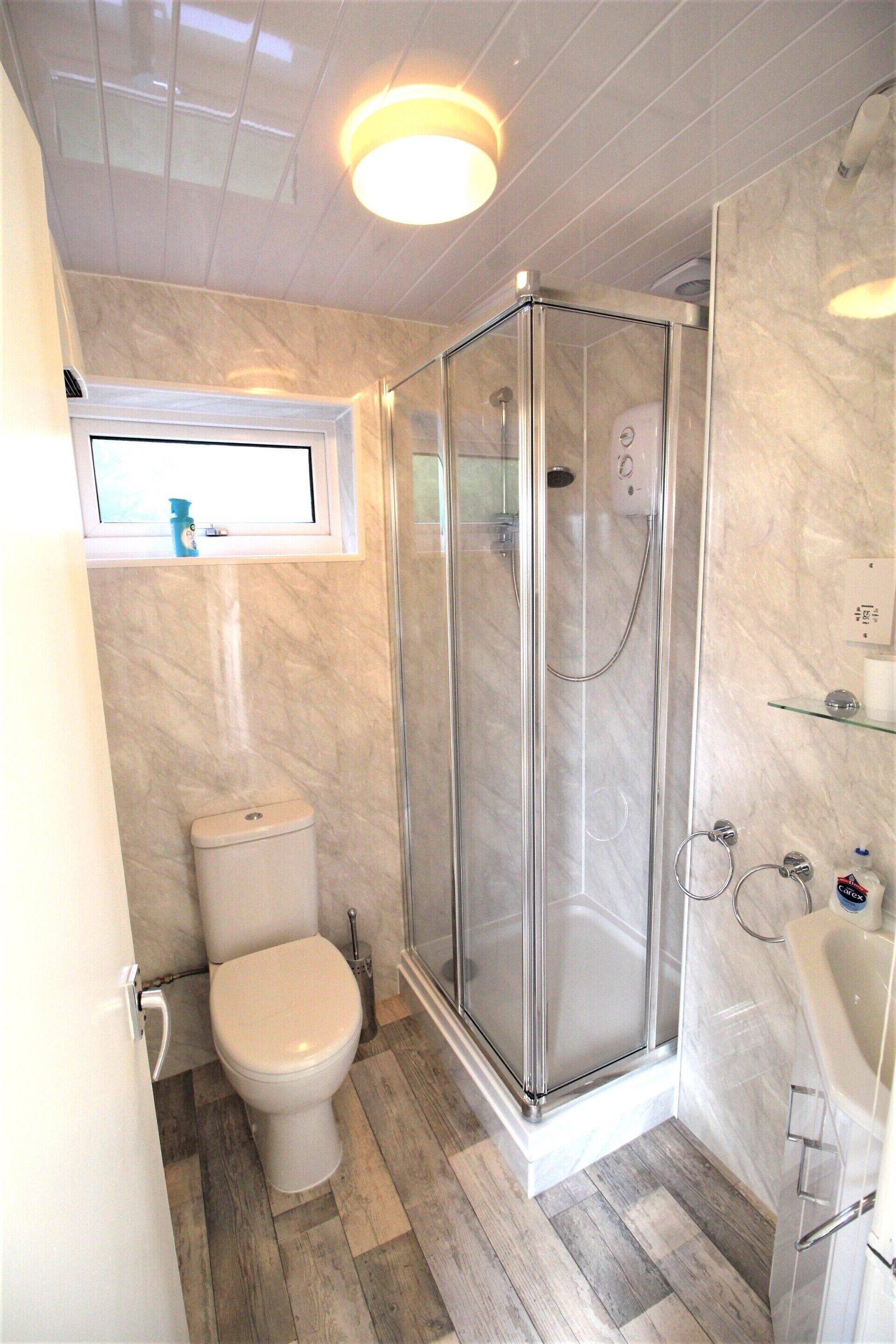 Une salle de bain comprenant des toilettes, une douche fermée par une paroi de verre et un lavabo.