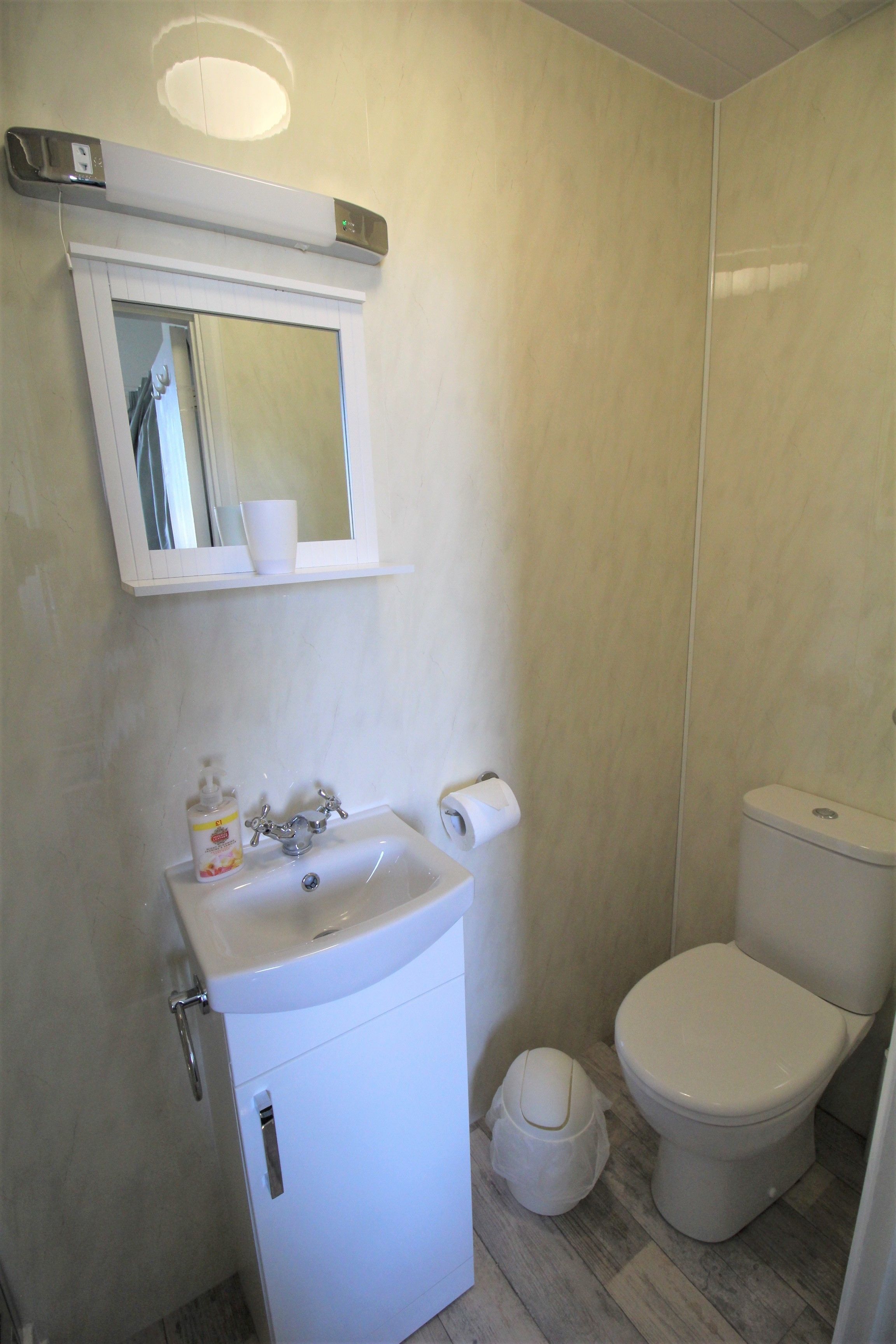 A bathroom with a sink, mirror, toilet, and a small trash bin.