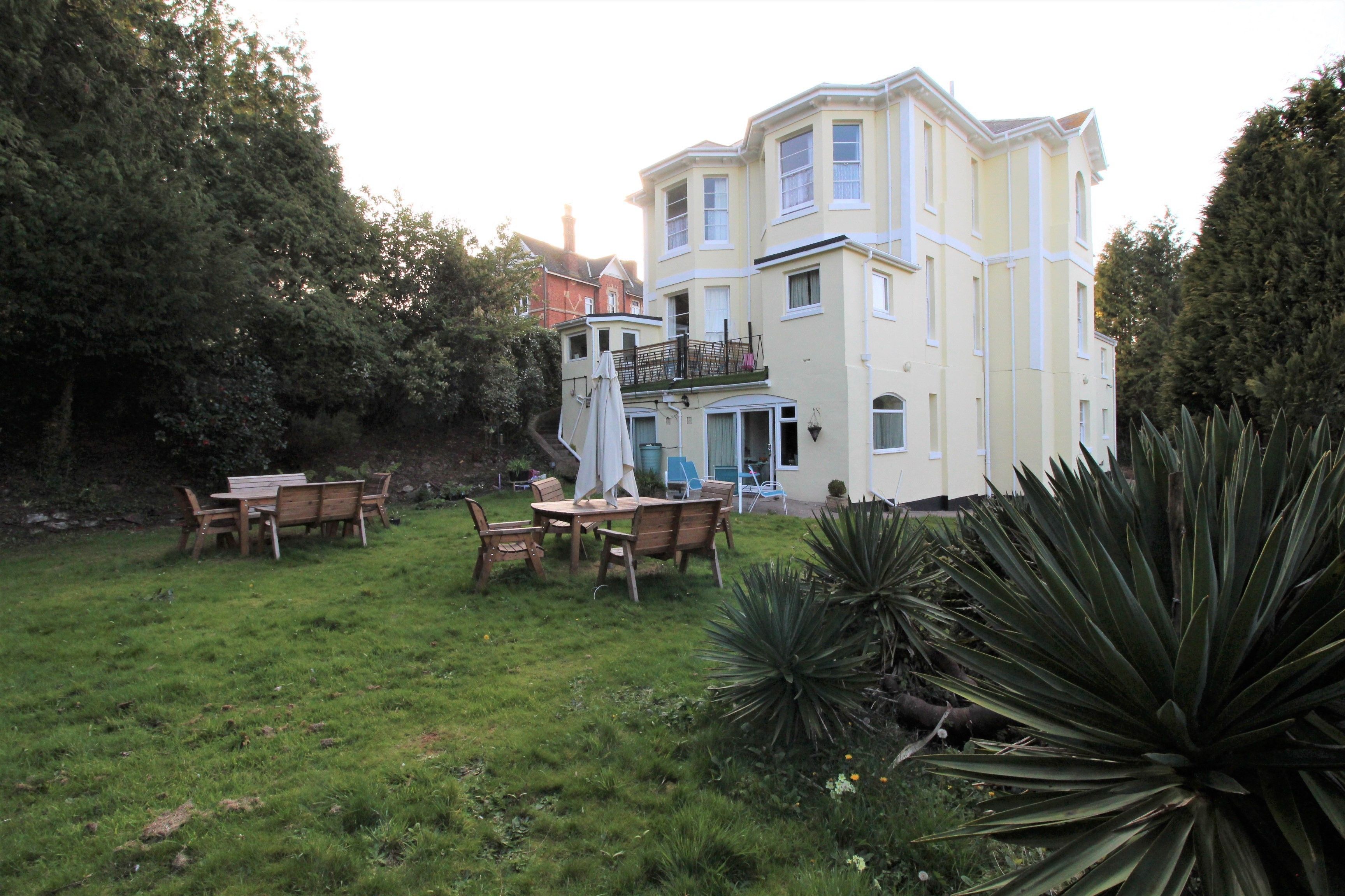 A large, multi-story building with a balcony and a well-maintained lawn with a wooden table and chairs.
