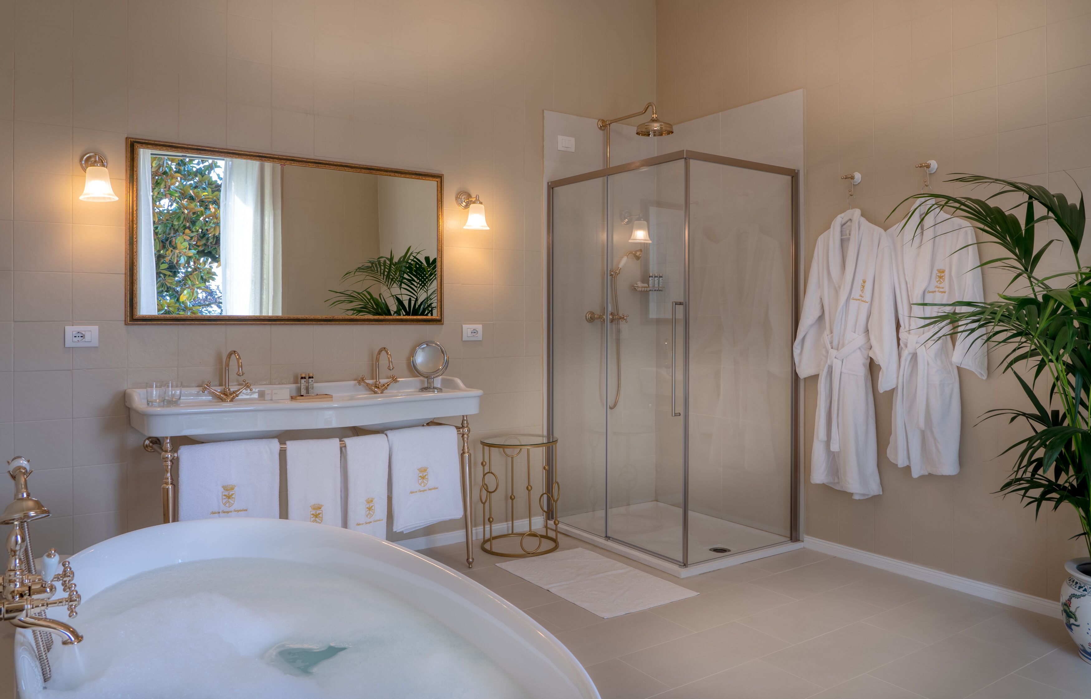 A bathroom with a bathtub, a glass-enclosed shower, a vanity with a mirror, and towels hanging on the wall.