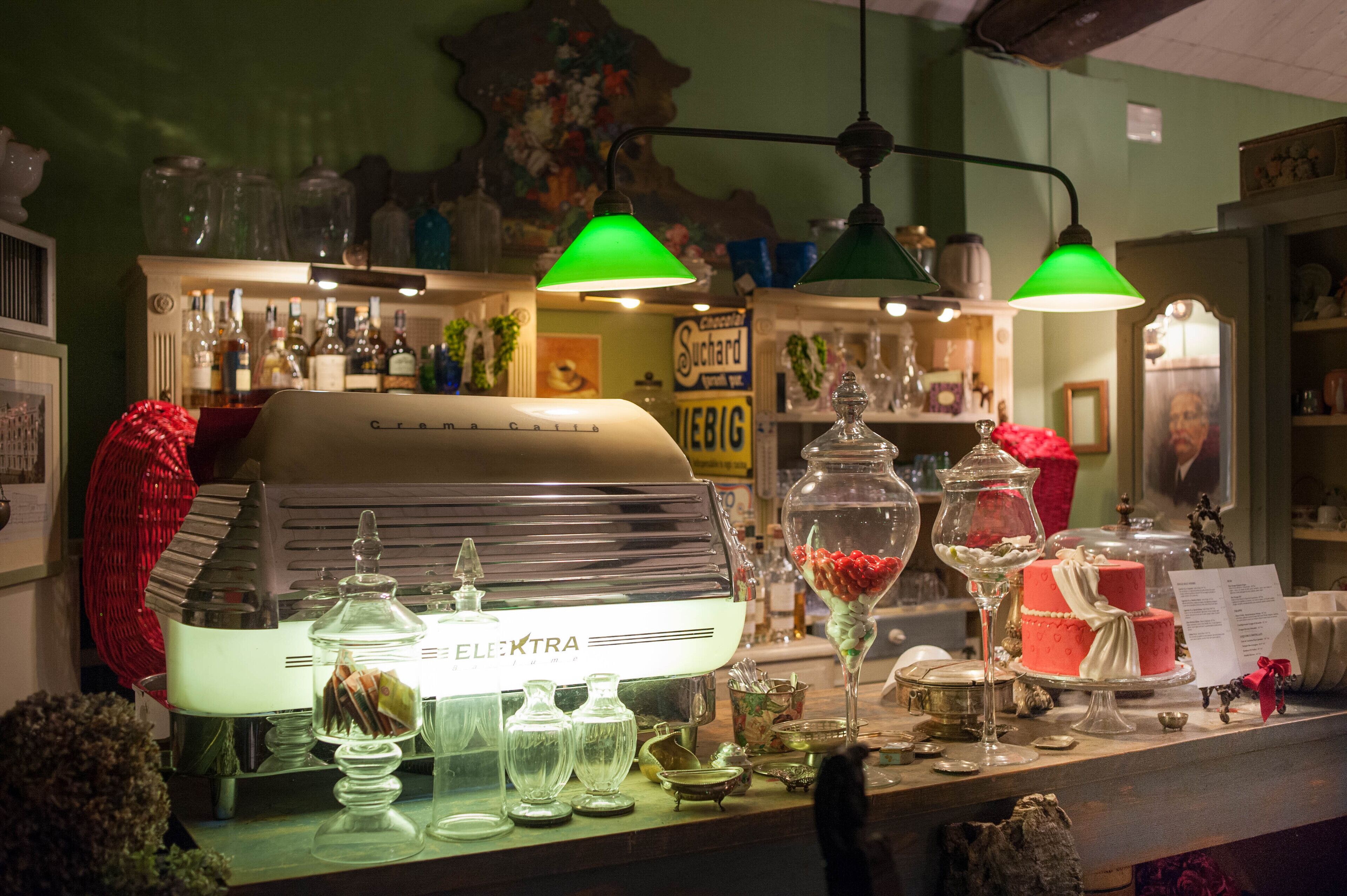 A bar area with a vintage espresso machine, glassware, and a cake on display.