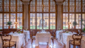 Un comedor con mesas dispuestas para cuatro, amplias ventanas en arco y vistas a un patio.