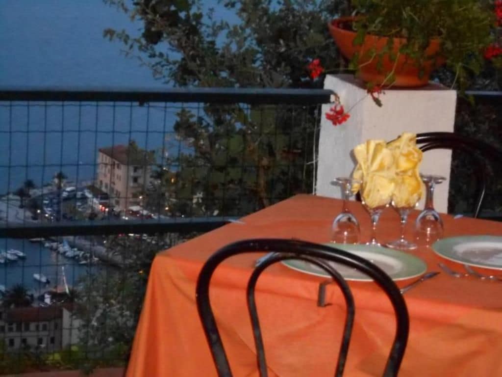 A table set with a tablecloth, a vase with a yellow flower, and wine glasses, overlooking a marina with boats and buildings.