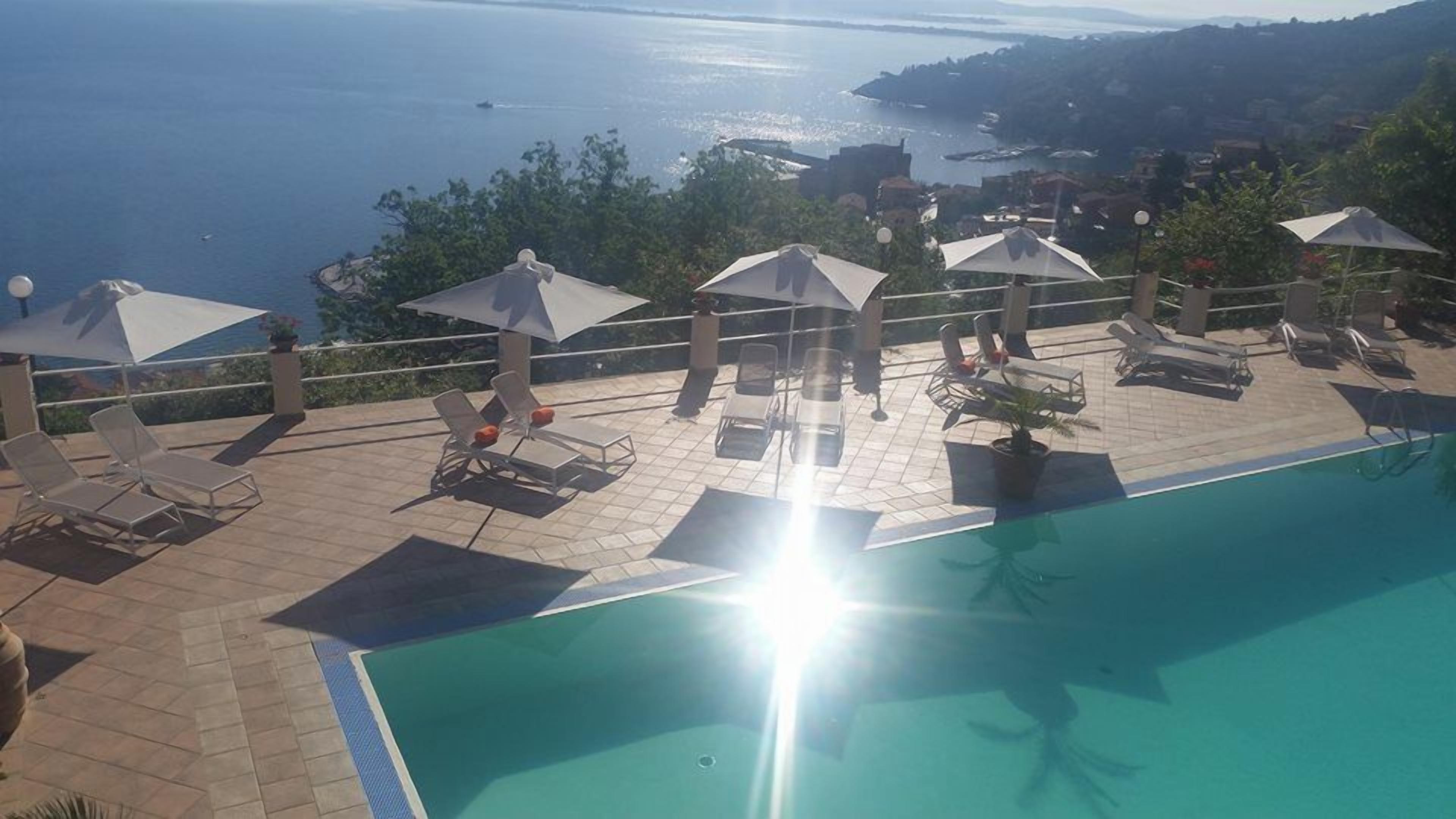 A poolside area with sun loungers and umbrellas, overlooking a body of water.
