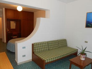 Una habitación con un sofá verde a cuadros, una mesita con una planta y una cama al fondo.