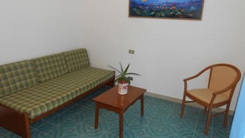A room with a checkered sofa, a wooden chair, a small table with a plant, and a tiled floor.