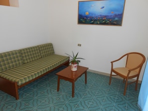 A living room with a checkered sofa, a wooden table with a plant, and a wooden chair. - Vittoria Porto Santo Stefano (Monte Argentario)