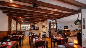 A restaurant with wooden beams, tables with red tablecloths, and a cozy interior.