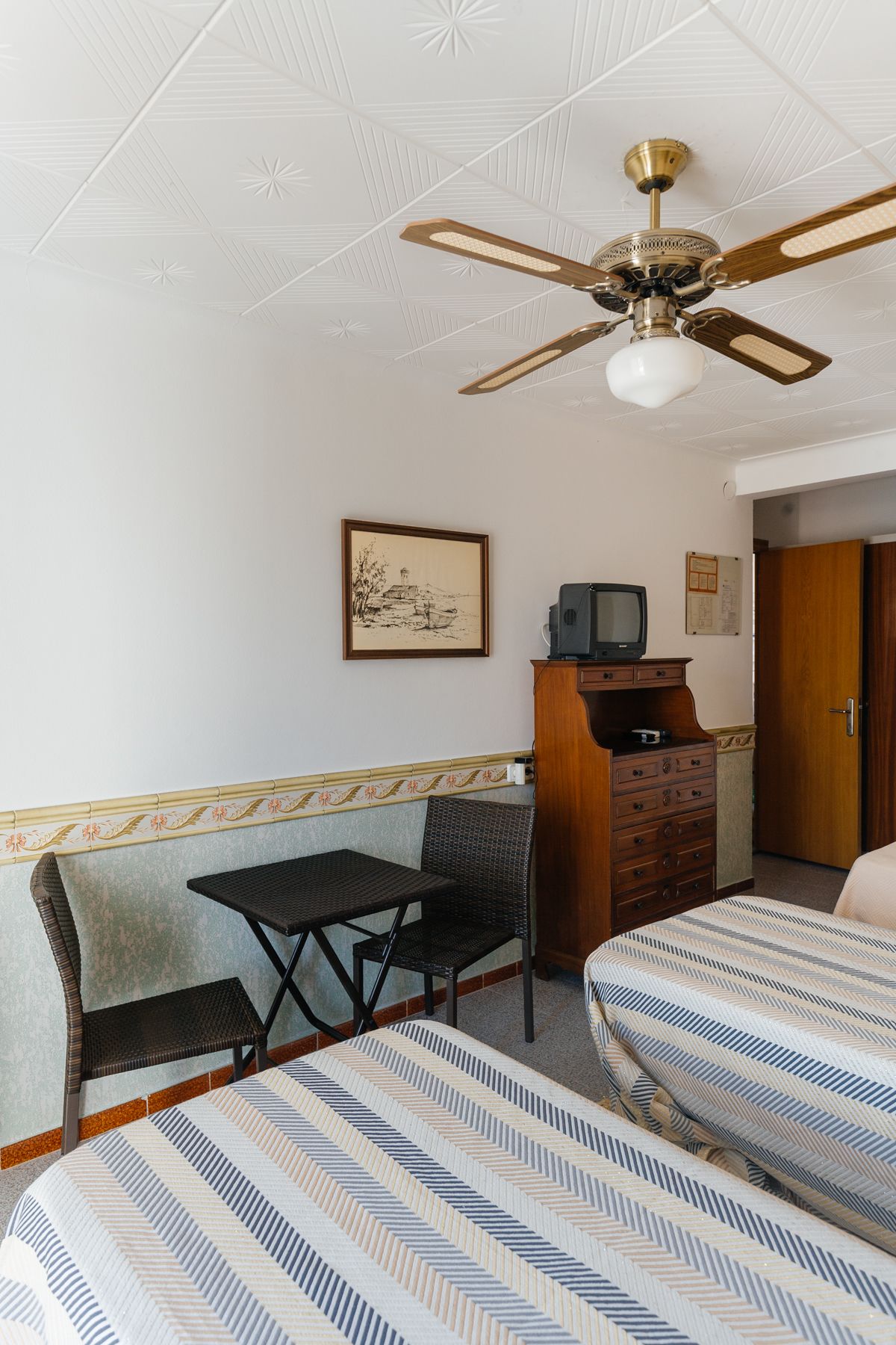 Una habitación de hotel con una cama, un escritorio, una silla, un televisor y un ventilador de techo.
