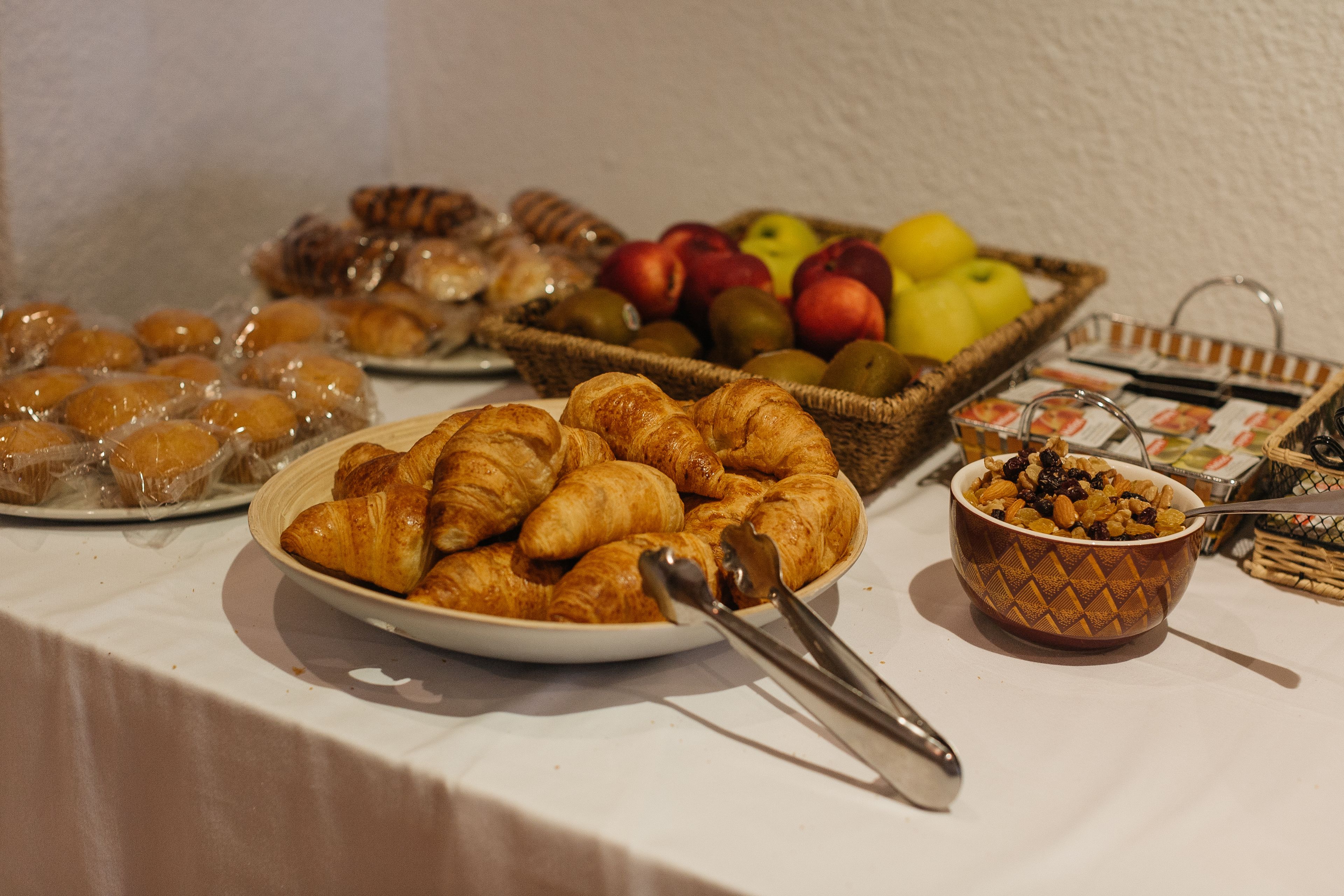 Ett buffébord med olika sorters mat, inklusive croissanter, frukt och en skål med nötter.