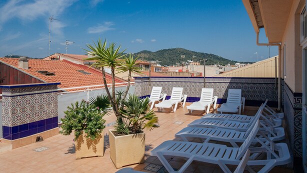 A rooftop terrace with white lounge chairs, potted plants, and a view of the cityscape and hills.