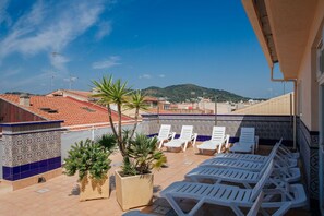 Terraza en la azotea con sillones blancos, plantas en macetas y vistas a la ciudad y las colinas.