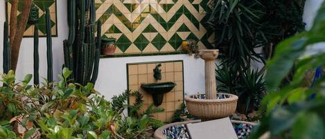 Un jardin avec des cactus, un mur recouvert de carreaux et une fontaine.