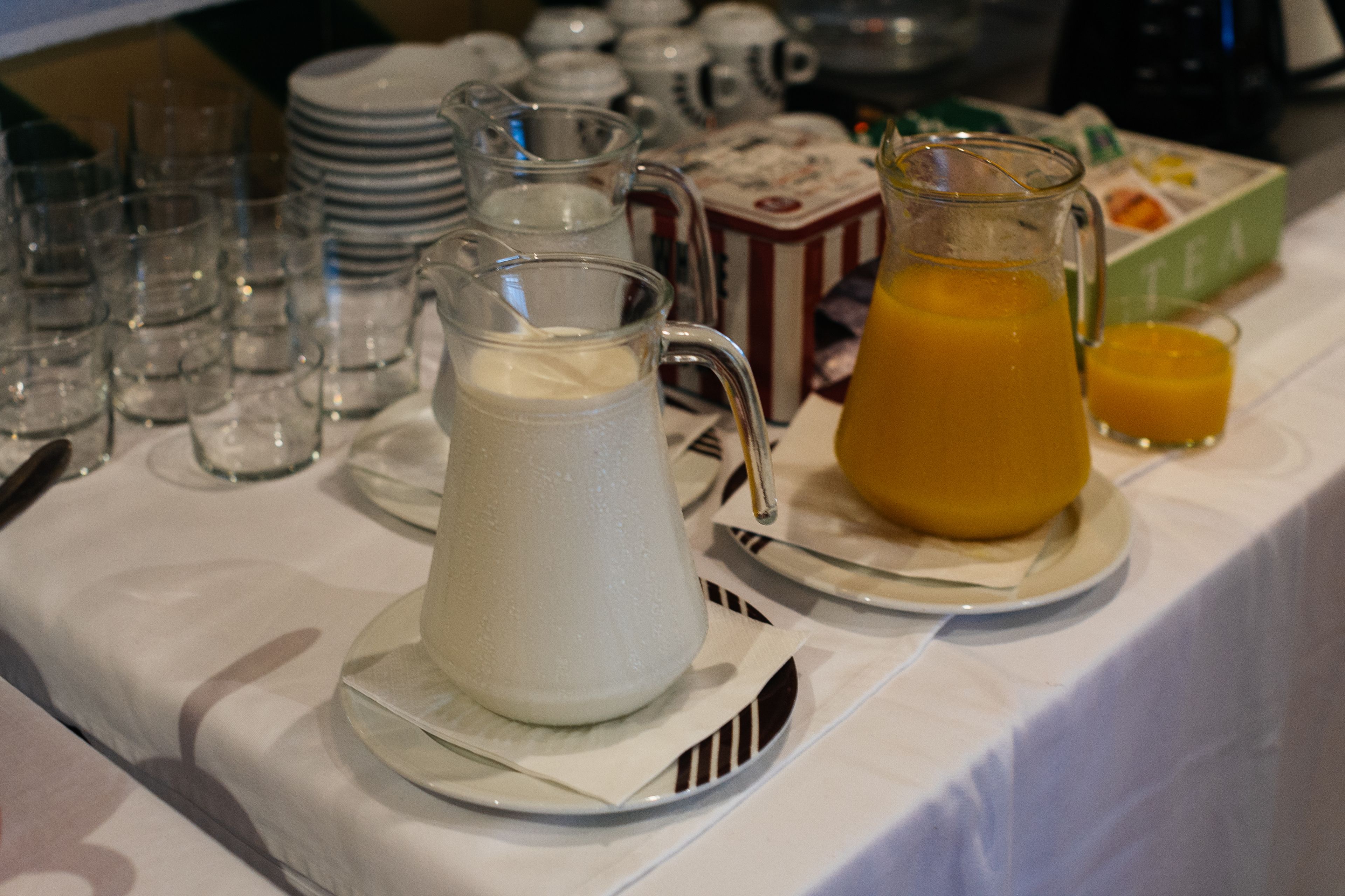 A breakfast table with a pitcher of milk, a pitcher of orange juice, and a box of tea.