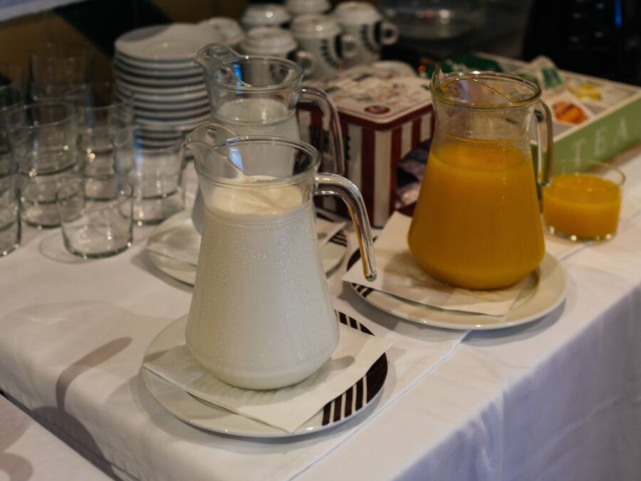 A breakfast table with a pitcher of milk, a pitcher of orange juice, and a box of tea.