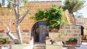 A stone building with a central archway, surrounded by potted plants and a tree. - Satori Gozo Centre (Xaghra)