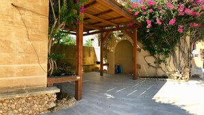A covered outdoor area with a stone wall, a wooden pergola, and a tiled floor. - Satori Gozo Centre (Xaghra)