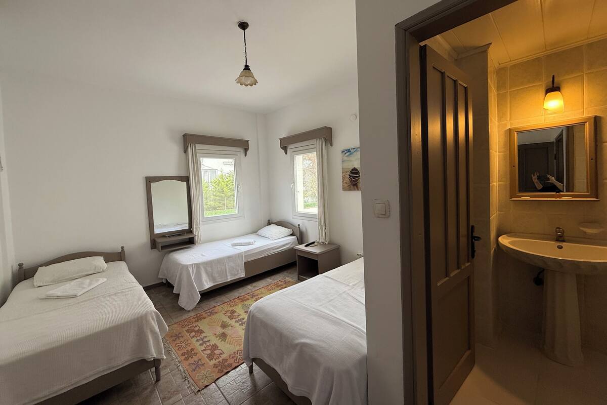 A bedroom with two beds, a window, a mirror, and a bathroom with a sink and mirror.