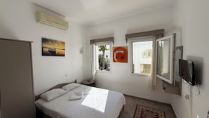 A bedroom with a bed, a nightstand, a TV, a window, and an air conditioning unit. - NEW SEDAN PANSIYON (Bodrum)