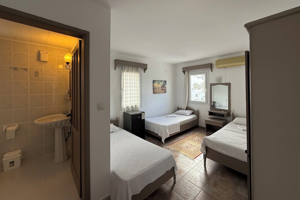 A bedroom with two beds, a bathroom with a sink, and a window with curtains.