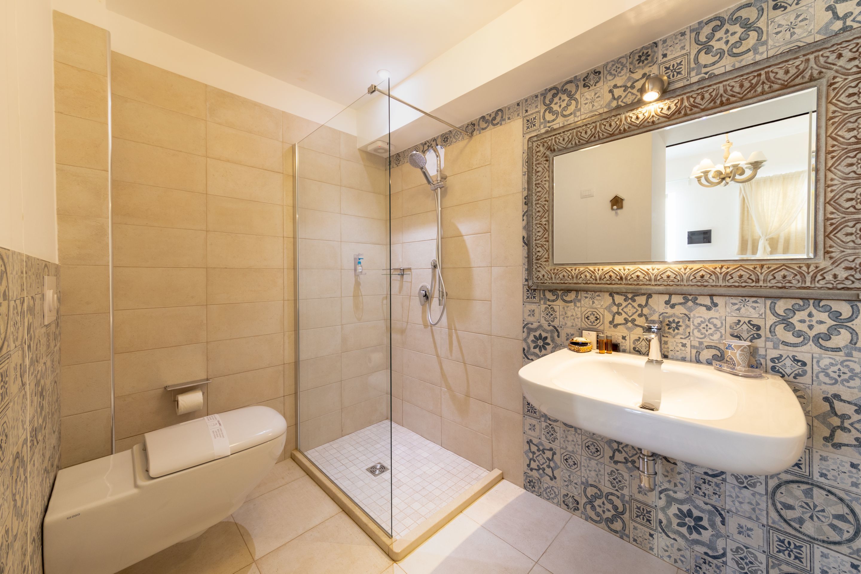 Un bagno con doccia vetrata, un lavandino bianco e piastrelle decorate.