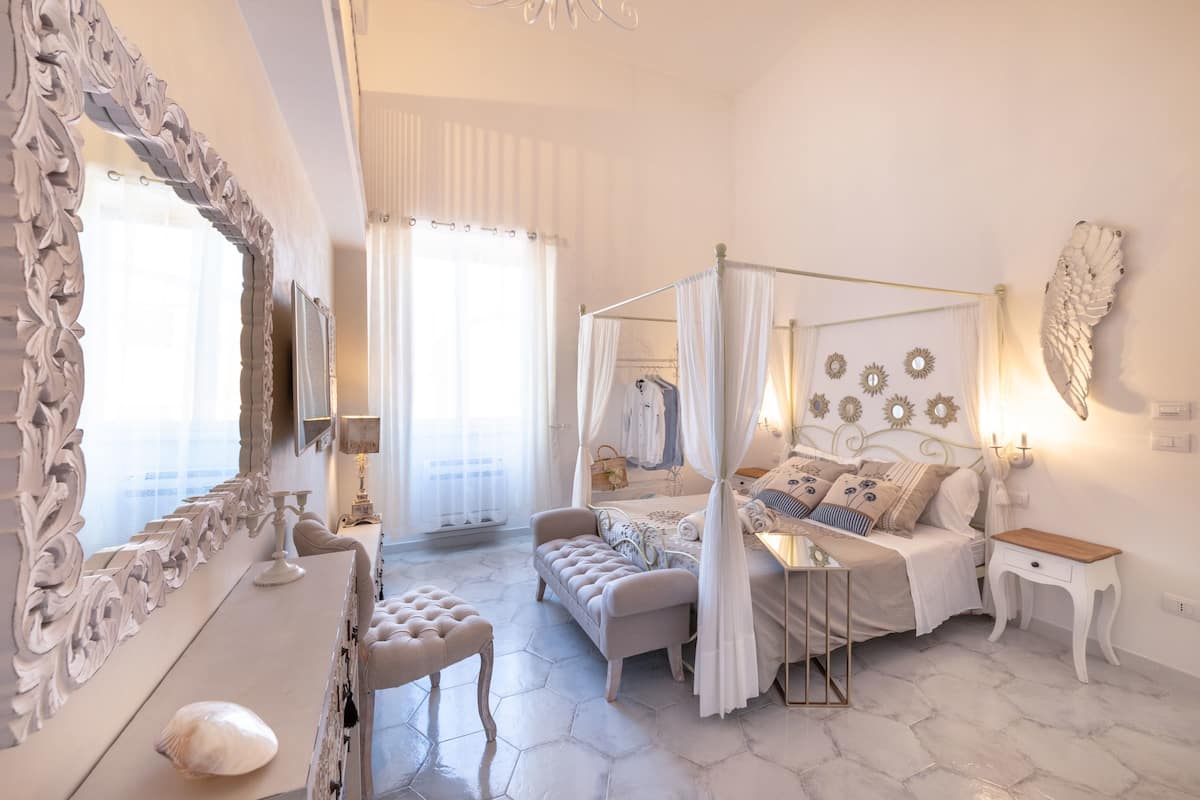 Quarto com cama de dossel, toucador com espelho, um banco e mesa de cabeceira.