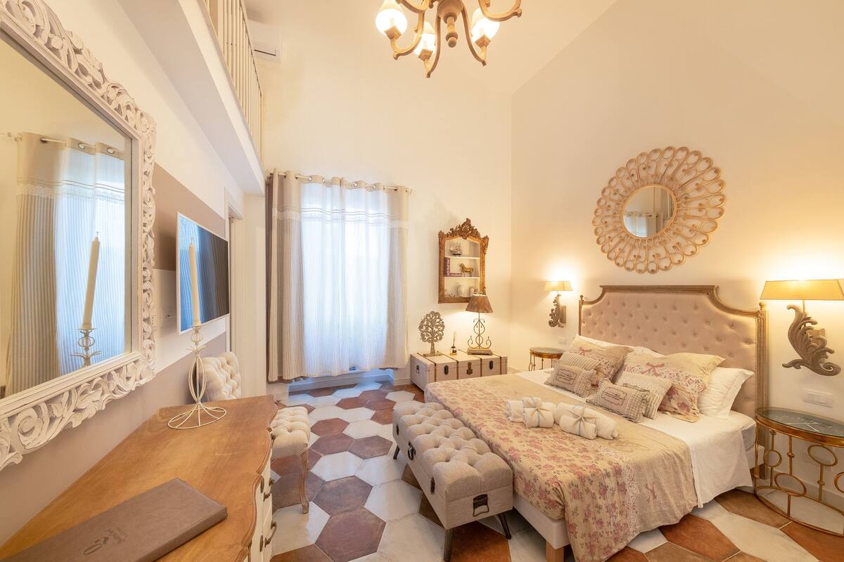 Quarto com uma cama grande, uma toucador com espelho, uma mesa de cabeceira e um candelabro.