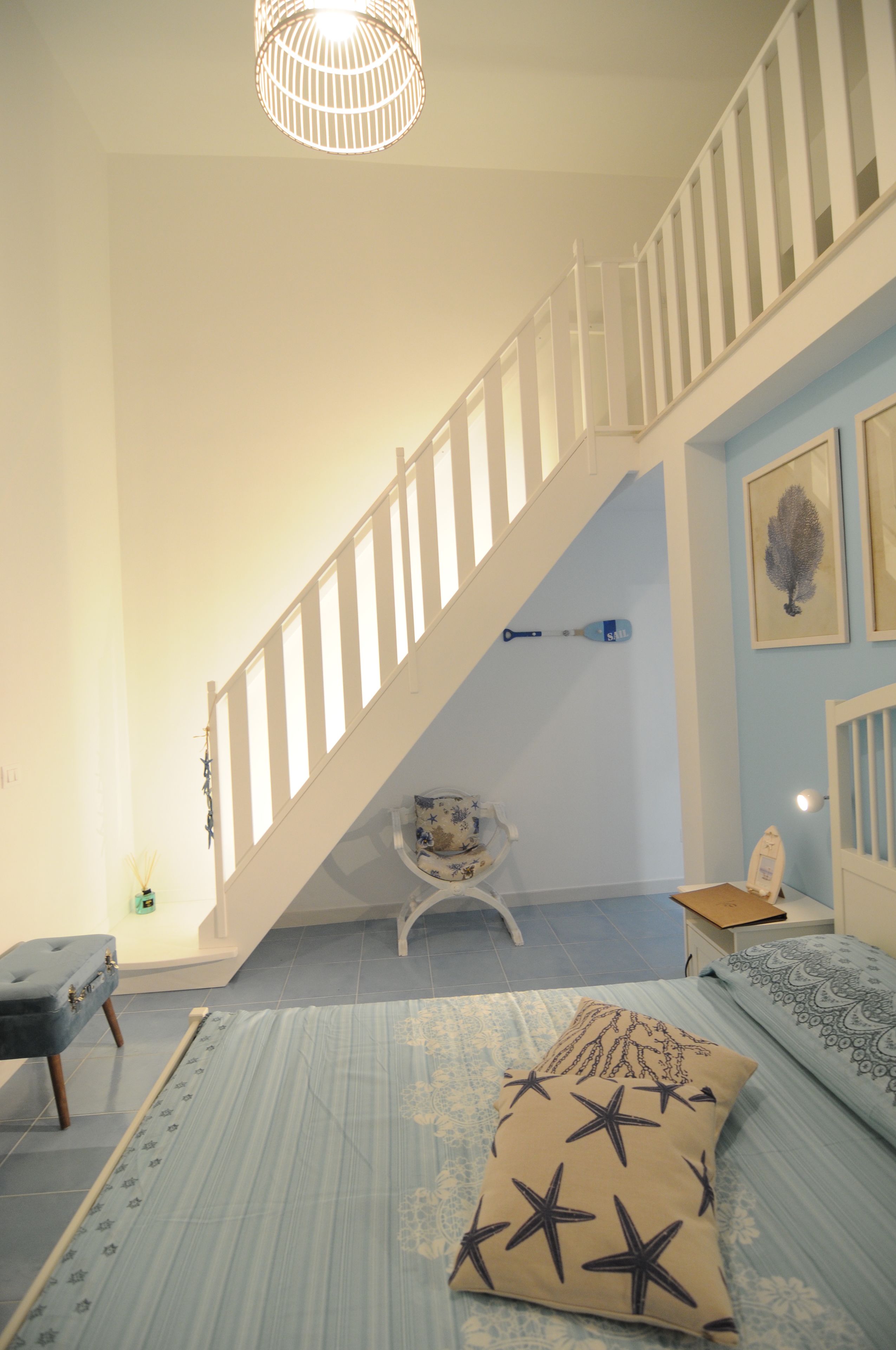 A bedroom with a staircase, a bed with a star-patterned pillow, a chair, and a hanging light fixture.