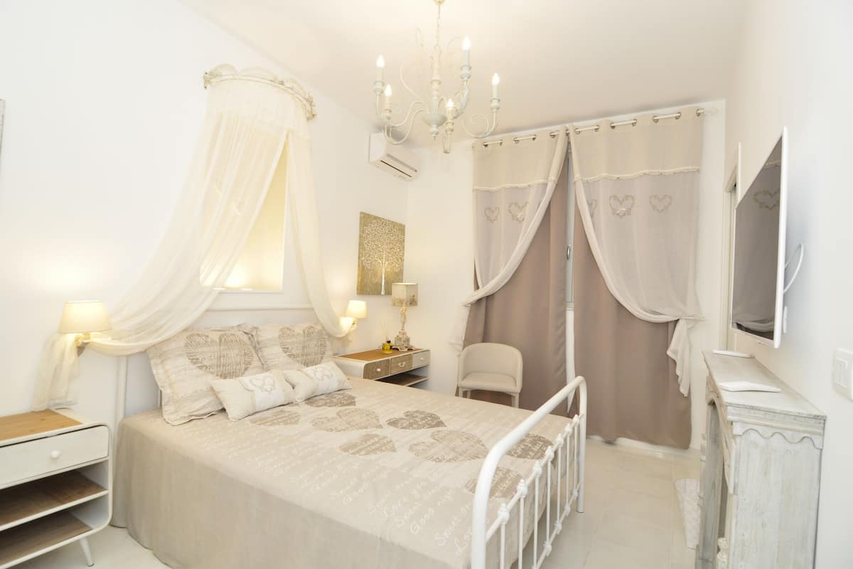 Um quarto com cama, mesa de cabeceira, luminária e espelho.