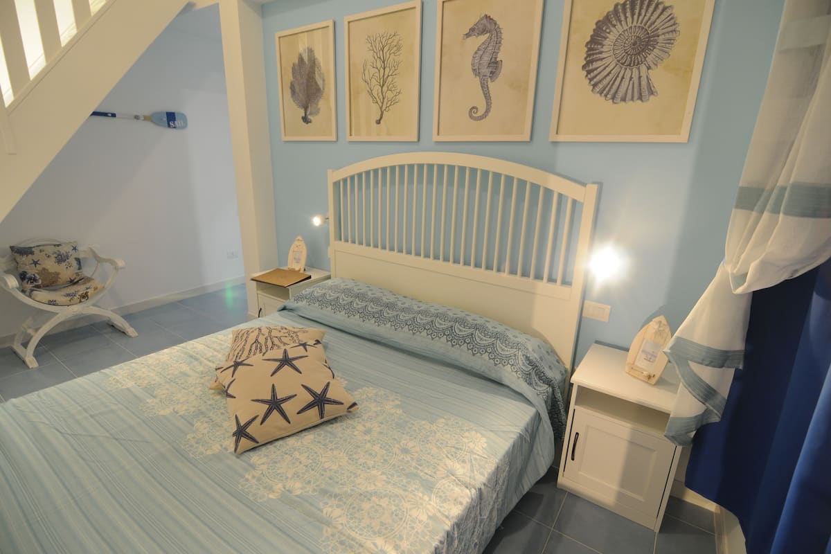 Quarto com cama, mesa de cabeceira, cadeira e decoração na parede.