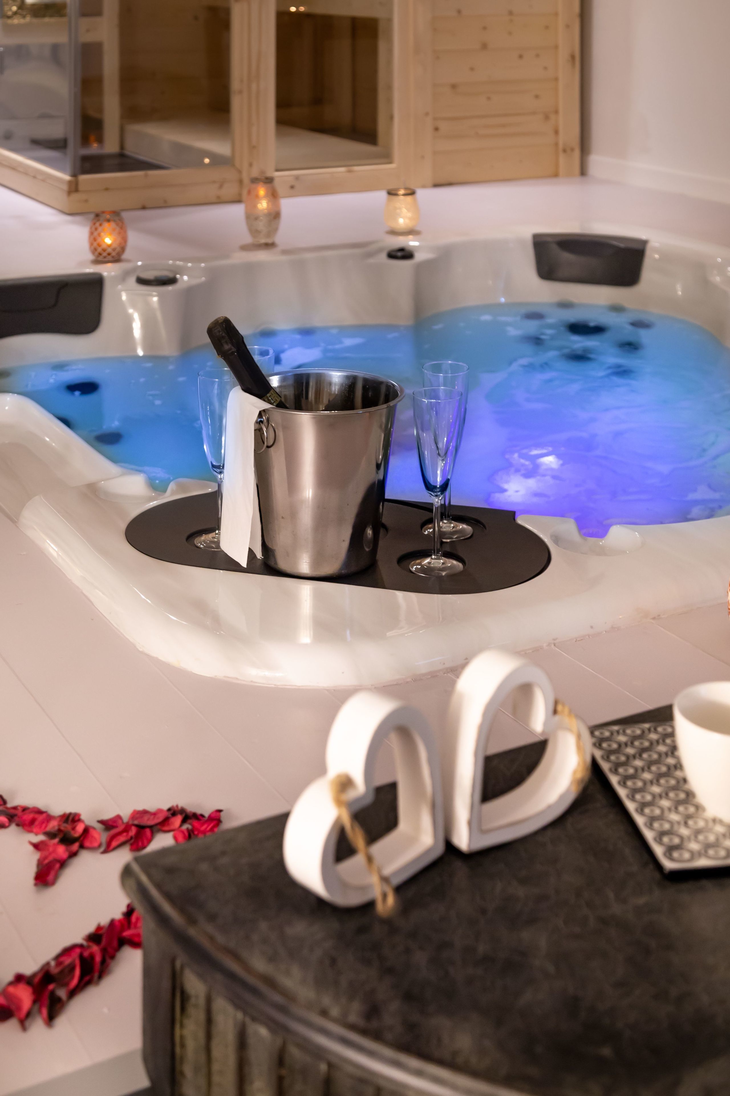 Un bain à remous avec un seau en métal et deux verres posés sur un tapis noir, le tout entouré de pétales de rose.