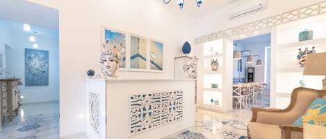 A spacious living area with a modern chandelier, a decorative wall panel, and a dining area in the background.