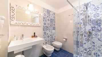 Un bagno con un lavandino bianco, un bidet, un water e una doccia rivestita di piastrelle azzurre a motivi decorativi.