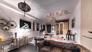 A modern living room with a brown sofa, a coffee table, and a fireplace. There are wall art pieces and a chandelier. - QuattroCuori Boutique Hotel & Spa (Portopalo di Capo Passero)