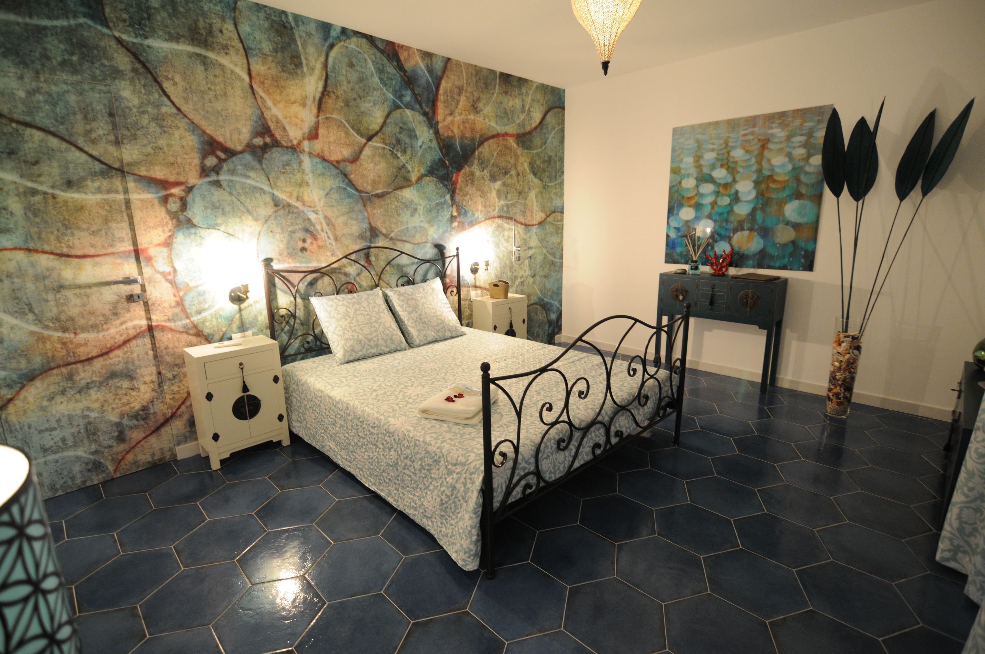 A bedroom with a bed, nightstands, a wall art piece, and a decorative vase.