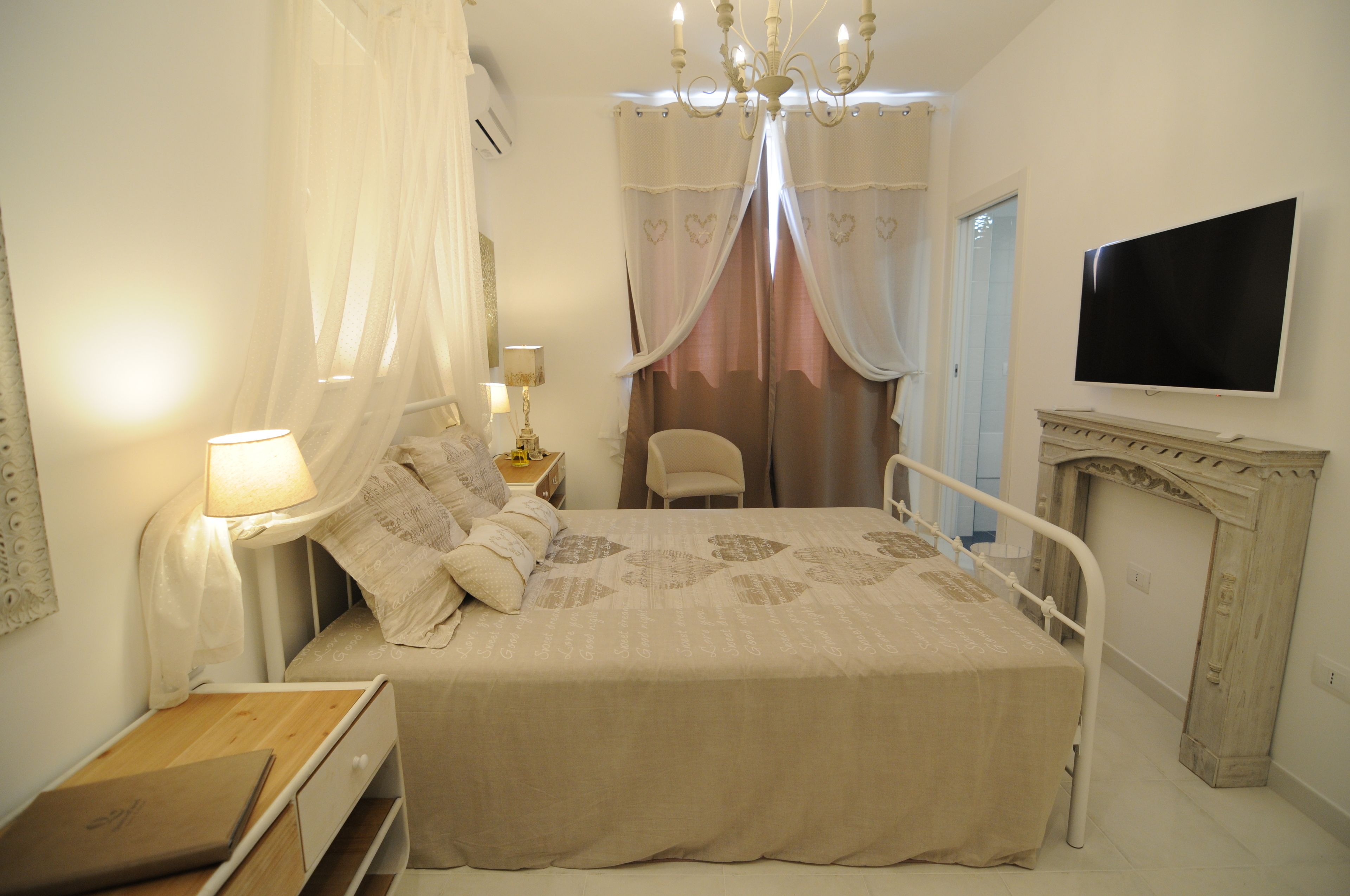 A bedroom with a bed, a bedside table, a lamp, a chair, a television, and a fireplace.
