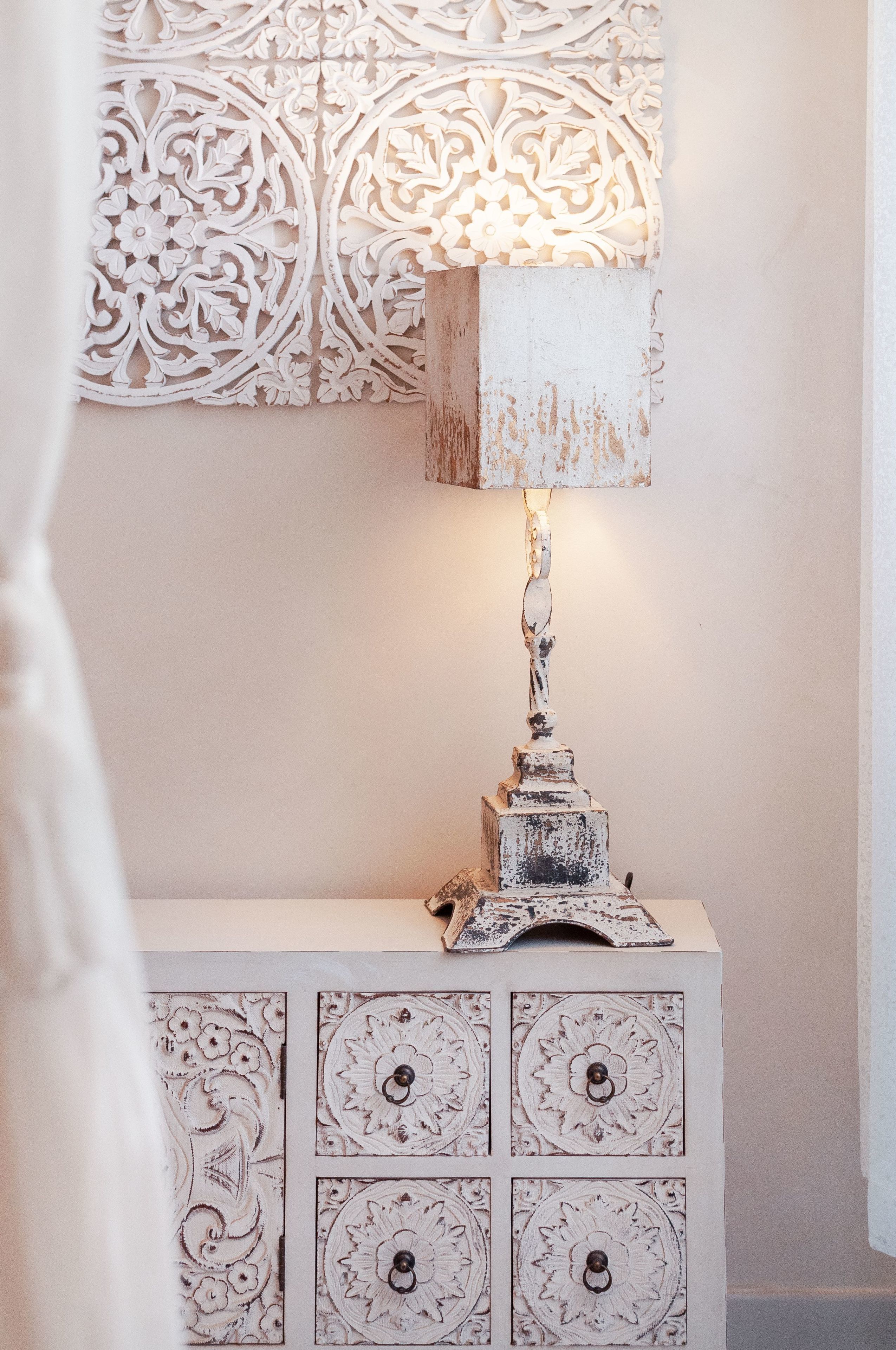 A white cabinet with intricate floral carvings and a lamp with a distressed finish.