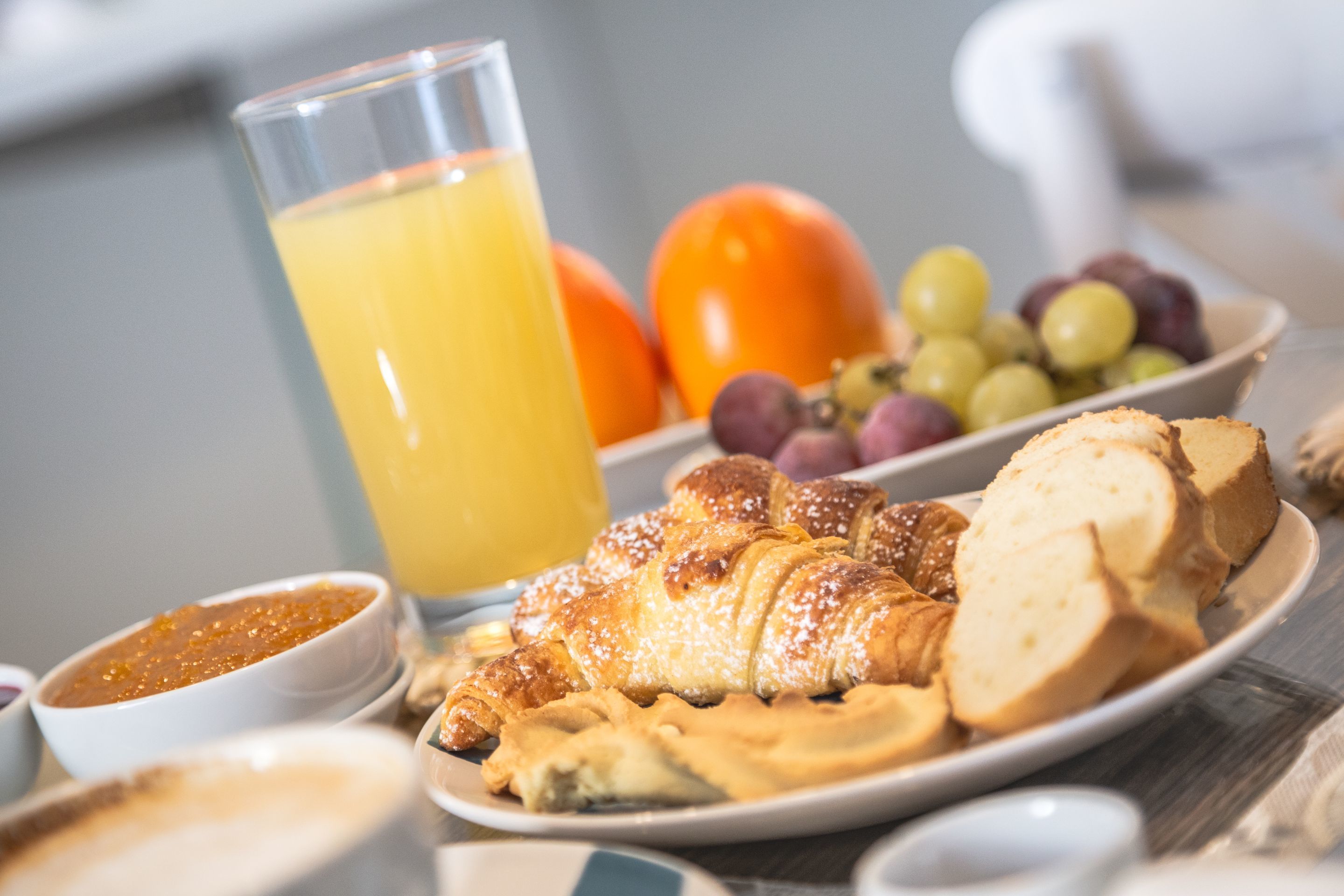 A breakfast setting with croissants, bread, fruit, and a glass of orange juice.