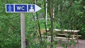Un panneau indicateur signalant l’emplacement des toilettes dans une zone boisée, à proximité d’une table de pique-nique.