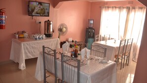 A dining area with tables set for four, a television mounted on the wall, and a water dispenser. - Sikalongo Lodge Highlands (Livingstone)