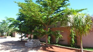 A tree-lined courtyard with a brick wall and a small palm tree. - Sikalongo Lodge Highlands (Livingstone)