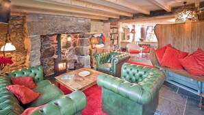 A cozy living room with green leather sofas, a stone fireplace, and a red carpet. - Tresillian, Beach House, Sea-views, Large Gardens (Sennen)