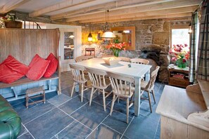 A rustic dining area with a stone wall, wooden furniture, and a stone fireplace. - Tresillian, Beach House, Sea-views, Large Gardens (Sennen)