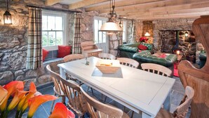 A rustic dining area with a stone wall, wooden furniture, and a fireplace. - Tresillian, Beach House, Sea-views, Large Gardens (Sennen)