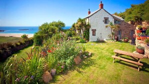 A stone house with a grassy garden and a bench, overlooking a beach. - Tresillian, Beach House, Sea-views, Large Gardens (Sennen)
