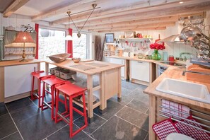 A kitchen with wooden countertops, a central island, red stools, and hanging utensils. - Tresillian, Beach House, Sea-views, Large Gardens (Sennen)