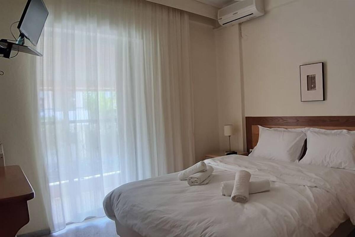 A hotel room with a large bed, a TV on the wall, and a window with curtains.